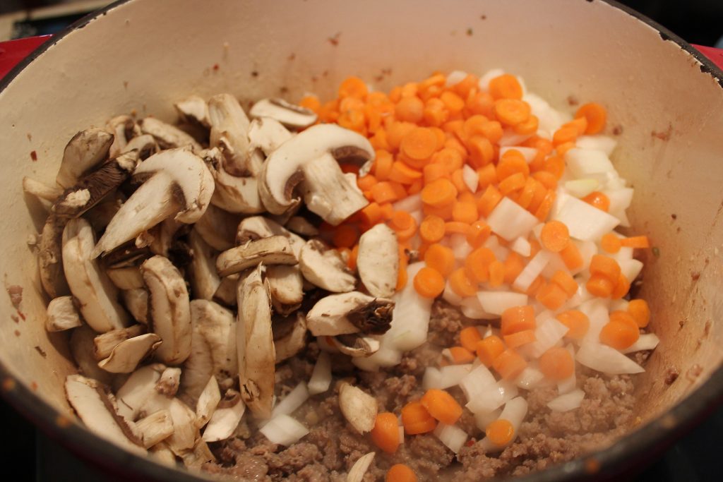 adding onions, carrots, and mushrooms to the pot