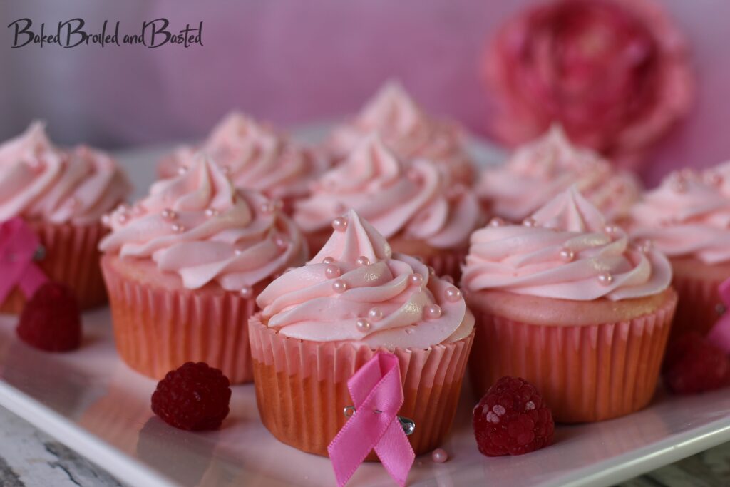 Pink champagne cupcakes with pink pearl sprinkles on a whiter platter with raspberries.