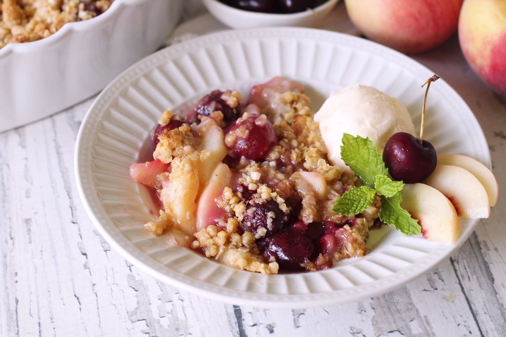 Peach and Cherry crisp in a white bowl topped with ice cream