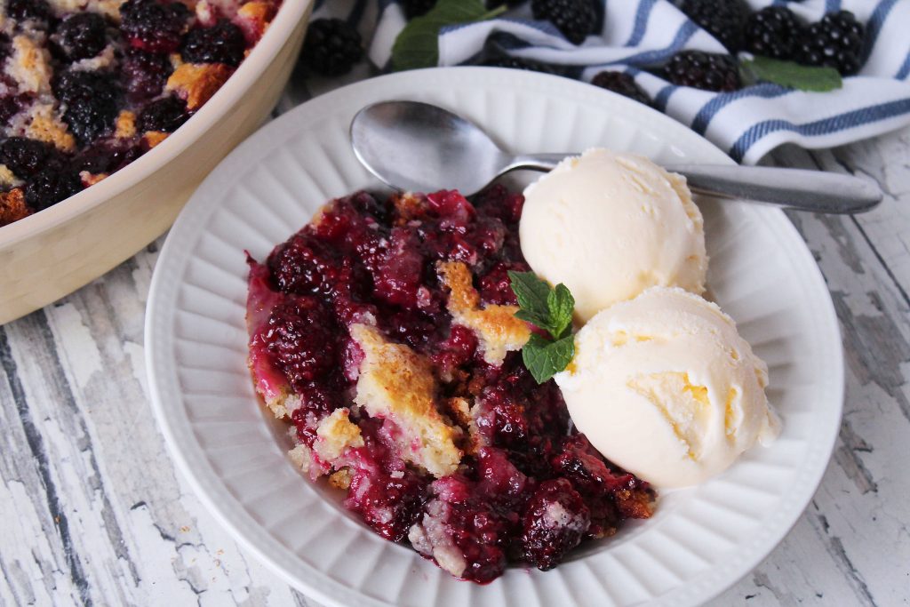 Blackberry cobbler and ice cream in a white bowl and spoon