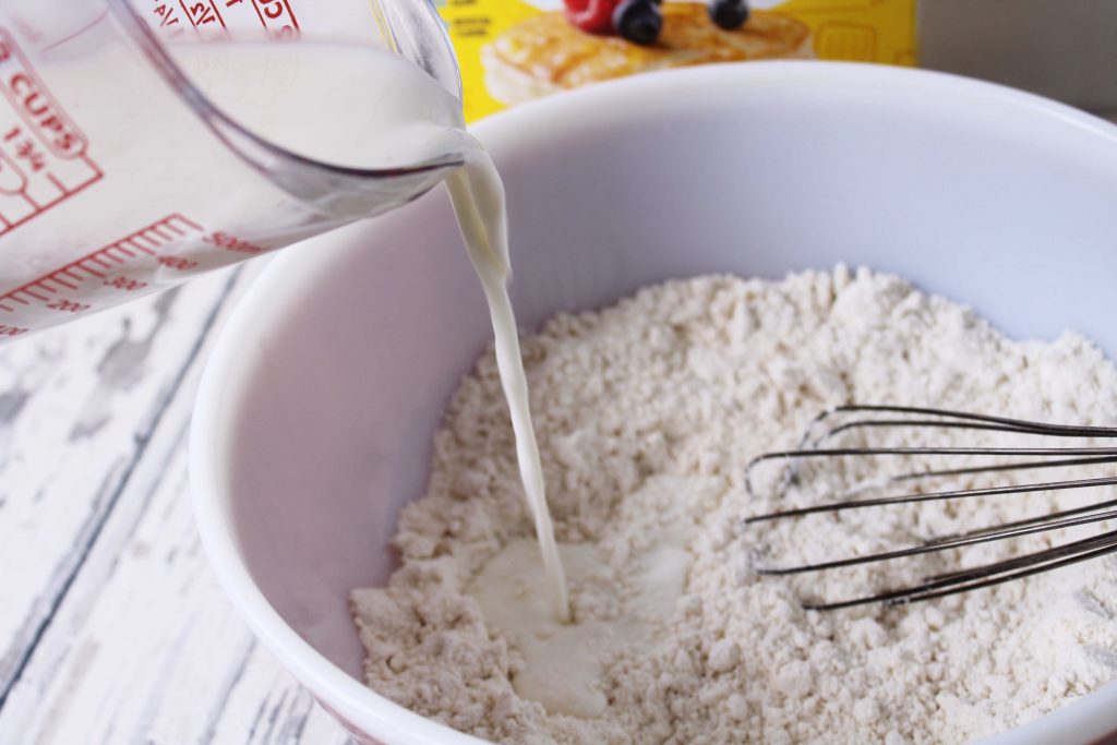 Pouring milk into mixing bowl that has bisquick and sugar in it 