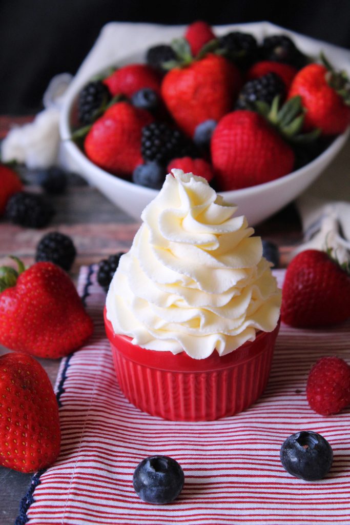Mascarpone whipped cream in a red cup surrounded by berries