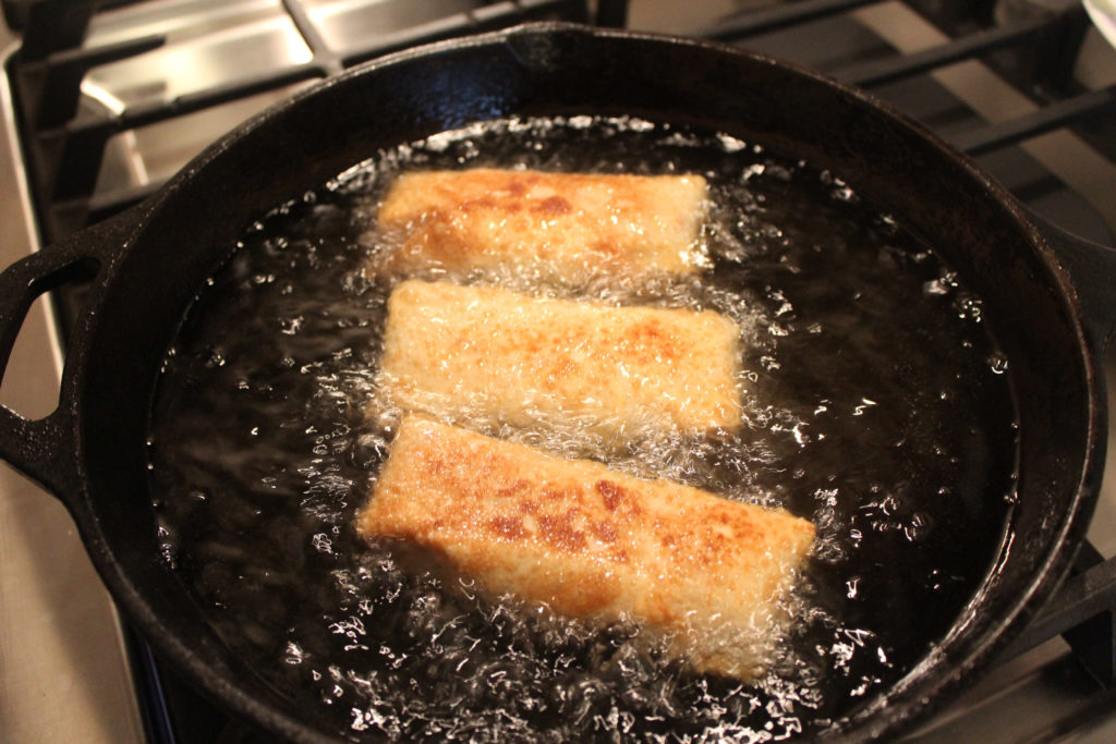 Golden brown egg rolls frying in a cast iron skillet