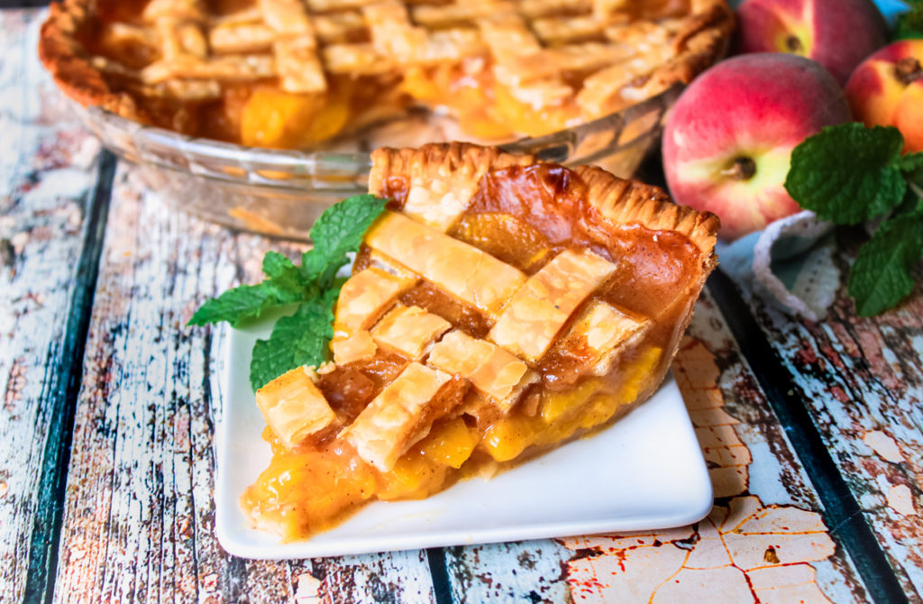 A slice of fresh peach pie on a white plate