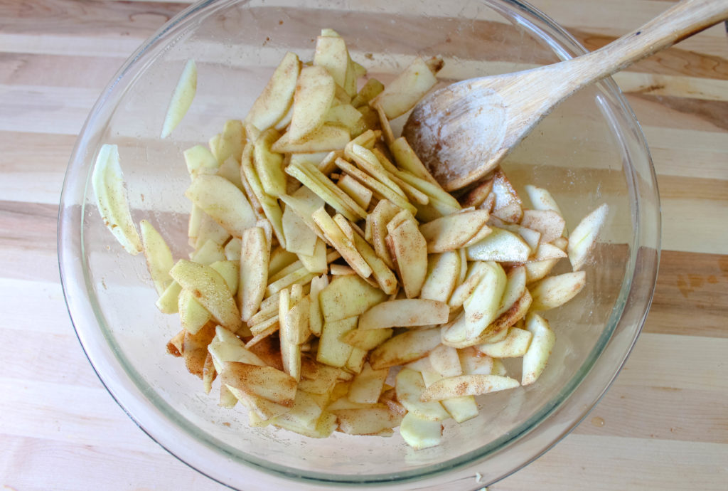 Sliced apples in a mixing bowl getting coated with filling ingredients