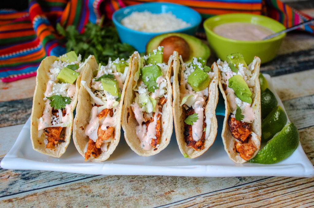 five fish tacos on a white plate. 