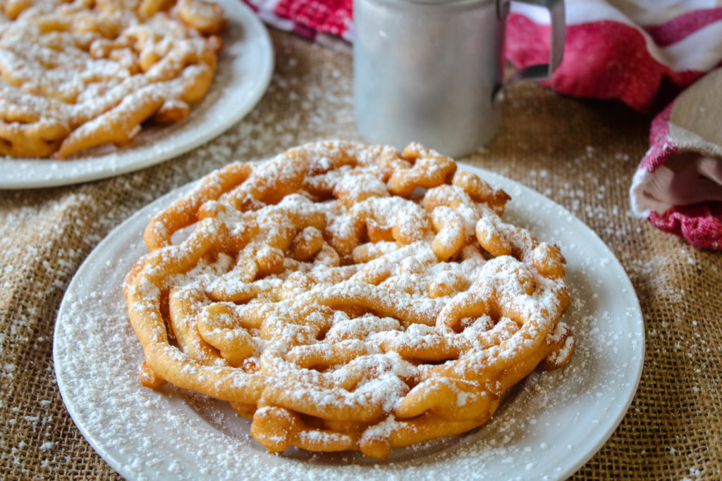 Two Fair Funnel Cakes on plated dusted with powdered sugar. 