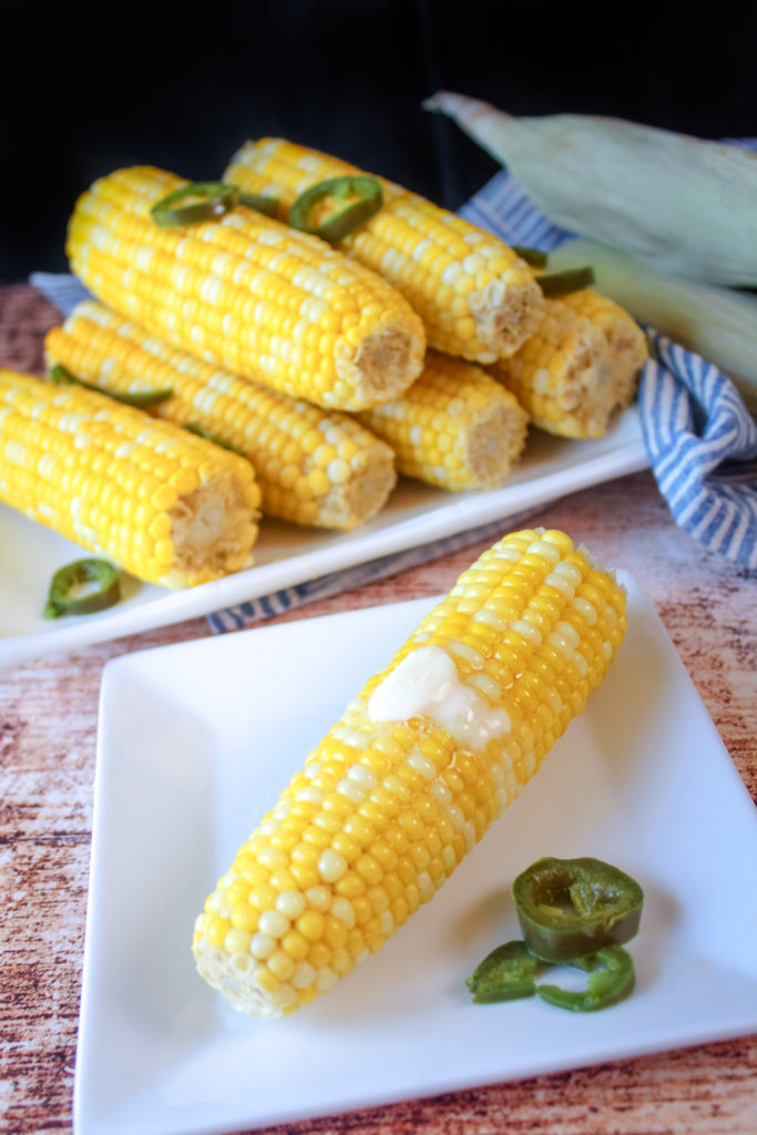 Boiled corn with honey and jalapenos on a white plate