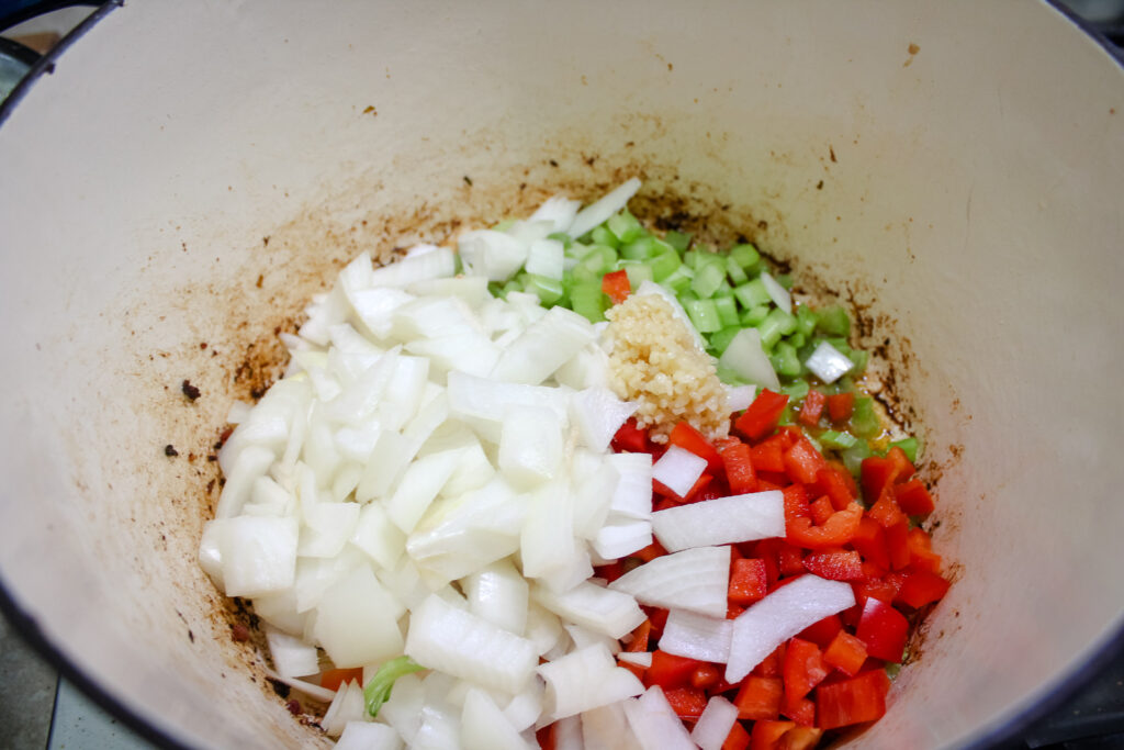 Adding the diced onions , diced bell pepper, diced celery and minced garlic to the soup pot to cook.
