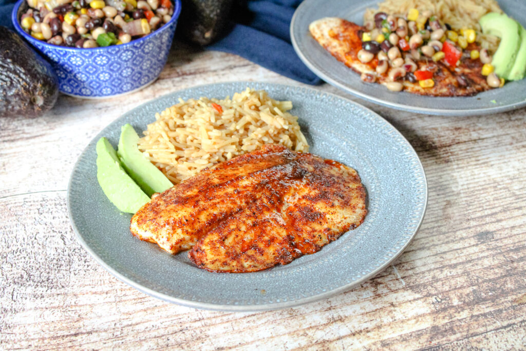 Southwestern Tilapia on a gray plate with rice and avocado slices. 