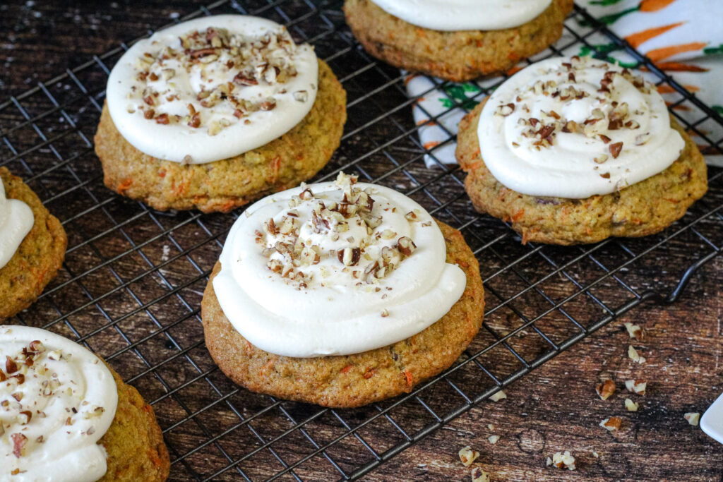 Crumbl Carrot Cake Cookies on a cooling rack frosted and with pecans on top