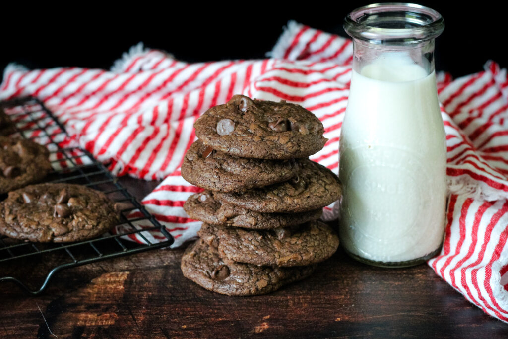 Brownie Mix Cookies stacked next to a glass of milk on a red and white striped towel. 