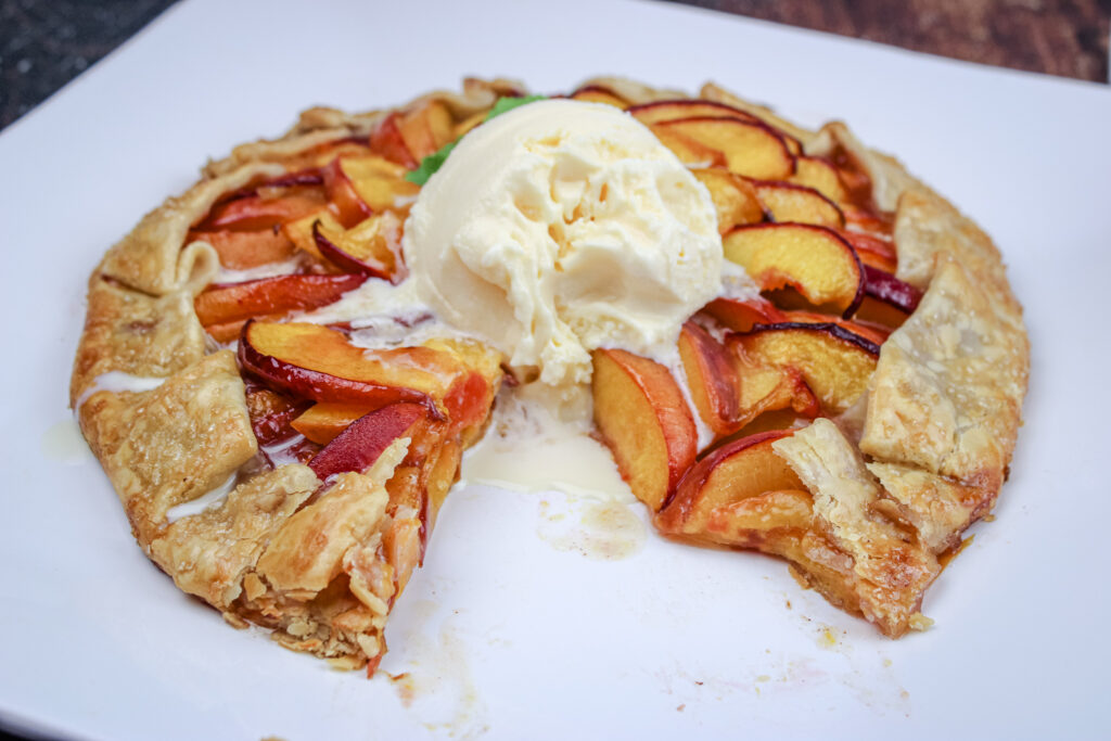Peach Galette baked with Ice Cream on top with a slice taken out . 