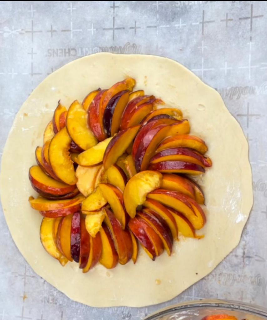 Pie Crust with peaches arranged on it for a peach galette 