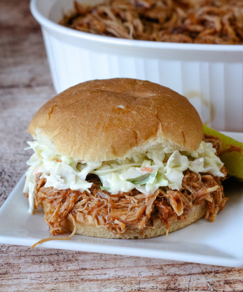 Slow Cooker Dr Pepper Pulled pork made into a sandwich with coleslaw on a white plate with a pickle 
