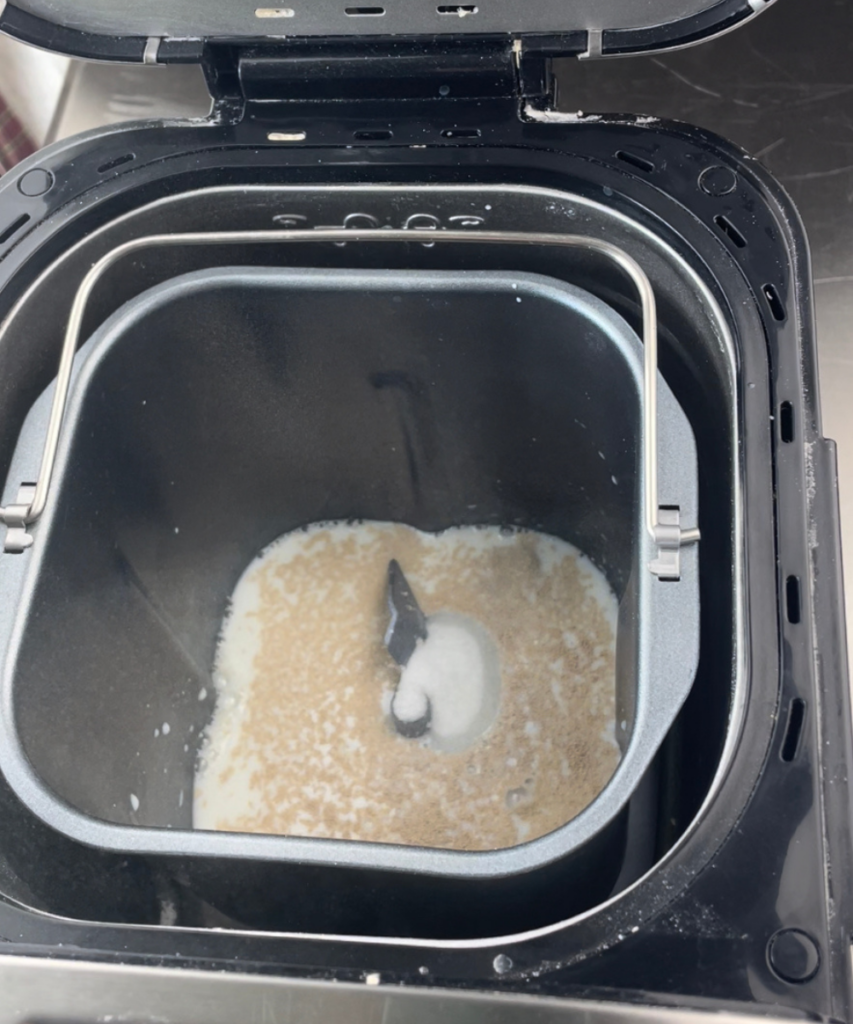 The well of the bread machine with the milk , sugar and yeast 
