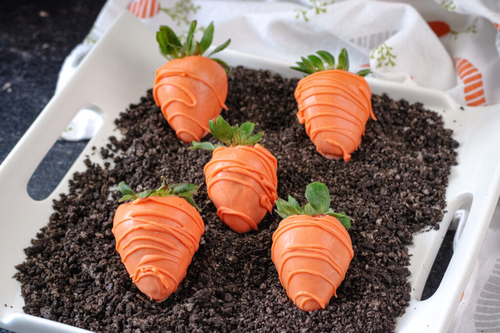 Candy coated strawberry carrots on a bed a crushed oreos to look like dirt. 