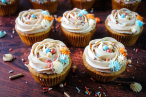 Pumpkin cupcakes with maple buttercream frosting with sprinkle pop sprinkles on top in blues , orange and cream