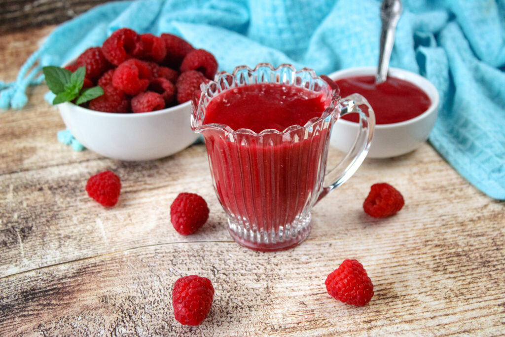 Raspberry sauce in a pouring cup with fresh raspberries around it 