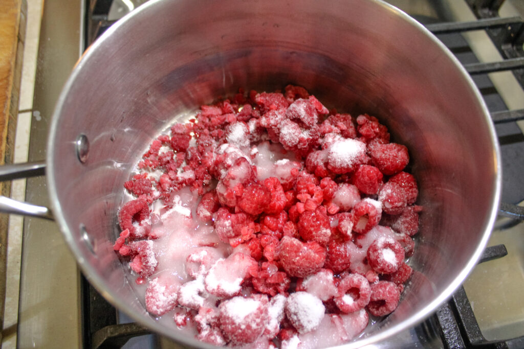Frozen raspberries in a pan with sugar , water and lemon juice 