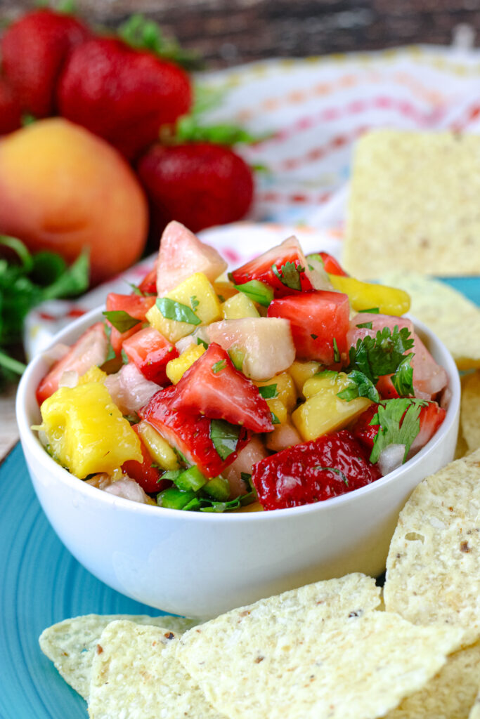 Fruit salsa in a white bowl placed on a turquoise plate with tortilla chips around it  