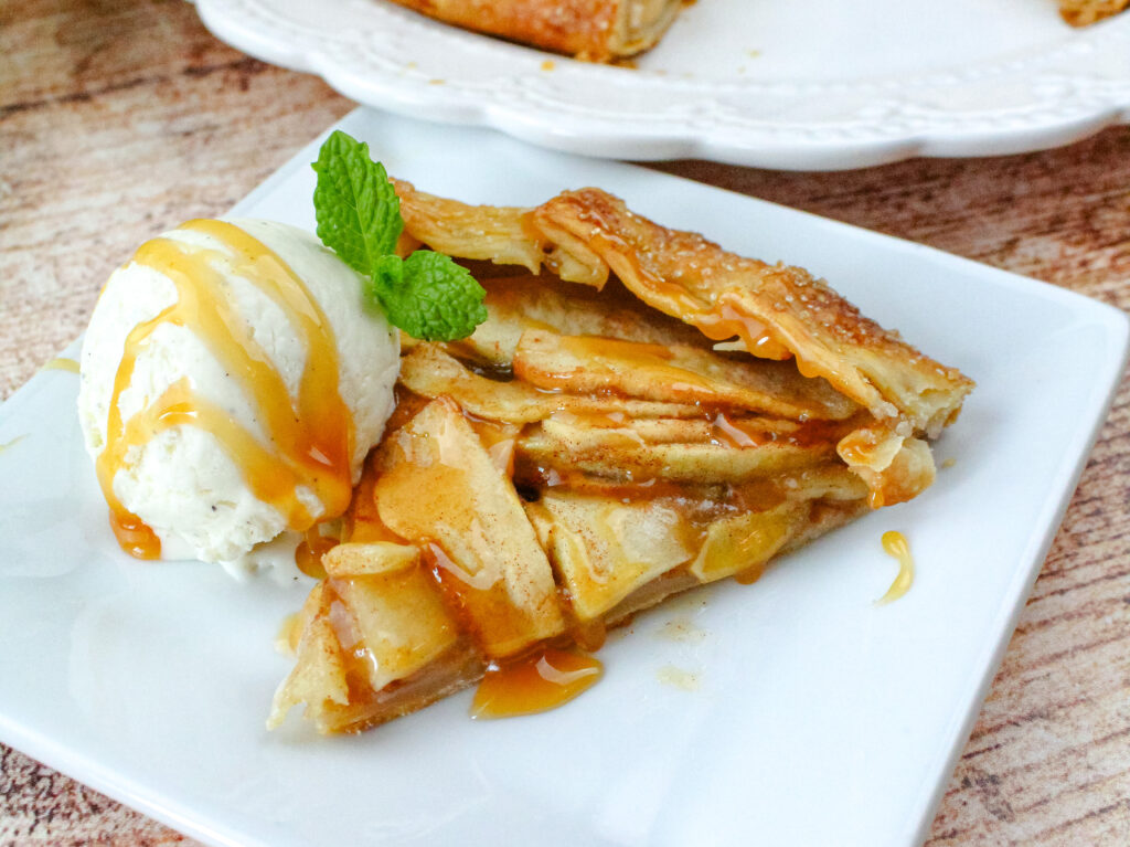 Caramel Apple Galette on a white plate with a scoop of ice cream with caramel drizzled on it . 