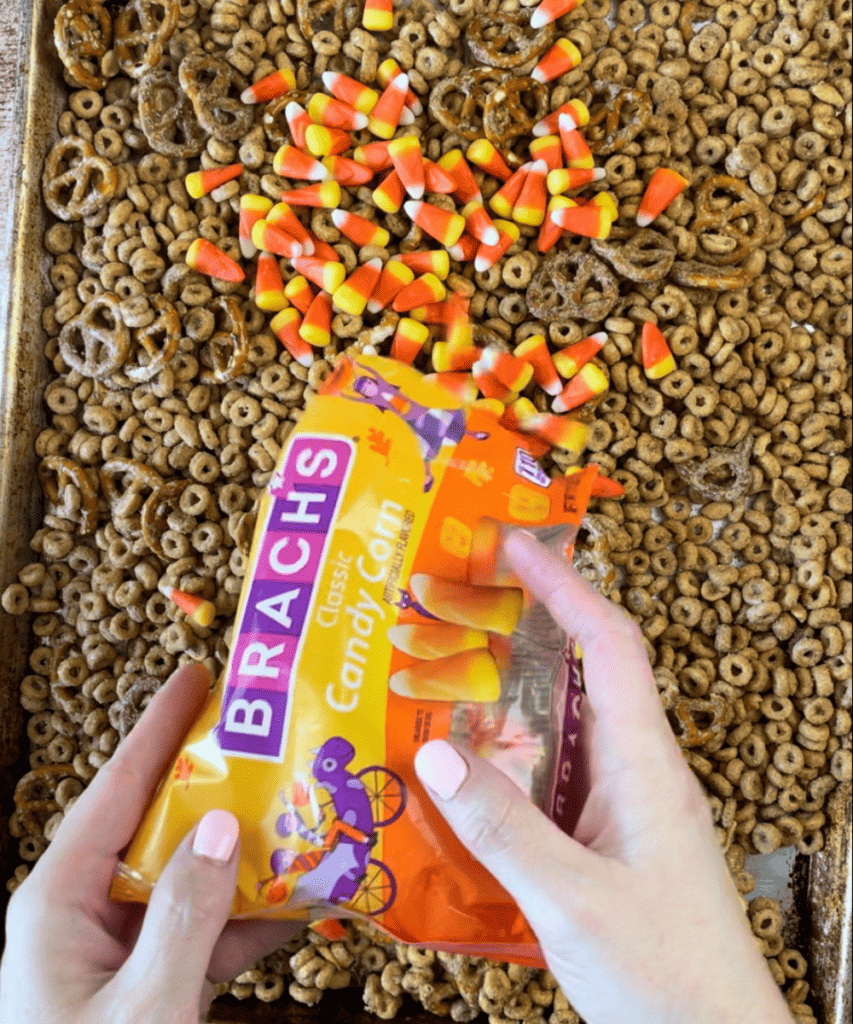 Candy corns being added to the pumpkin spice cheerios snack mix 