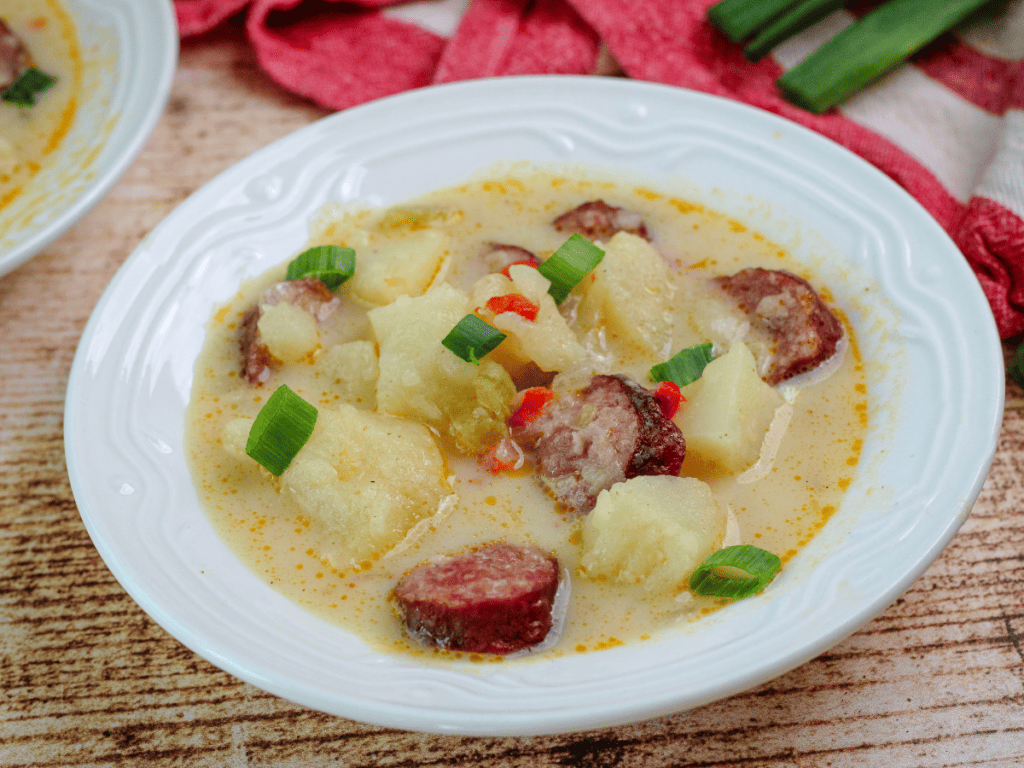cajun sausage potato soup in a white bowl with green onions on top 