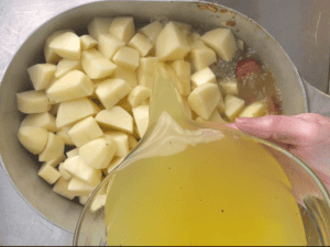 Adding the chicken broth to the pot for Cajun sausage potato soup