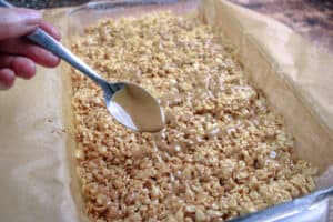 Melted cookie butter being drizzled over the top of cookie butter rice krispie treats