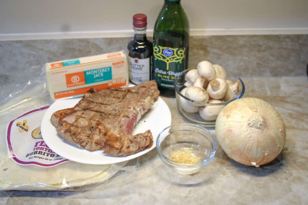 The ingredients for leftover steak quesadillas -leftover steak , tortillas , onion, garlic , mushrooms . monterey jack cheese , olive oil and red wine