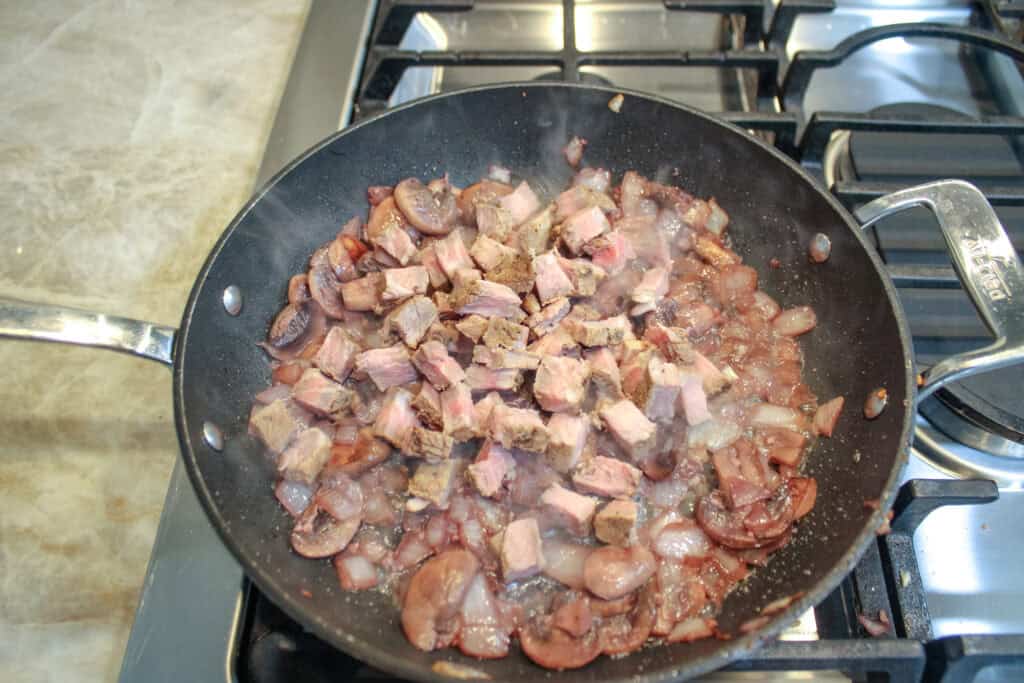Adding cubed leftover steak to onions, mushrooms and garlic in a skillet