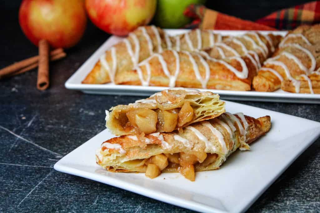 An apple turnover made with puff pastry sliced in half on a square while plate