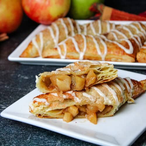 An apple turnover made with puff pastry sliced in half on a square while plate