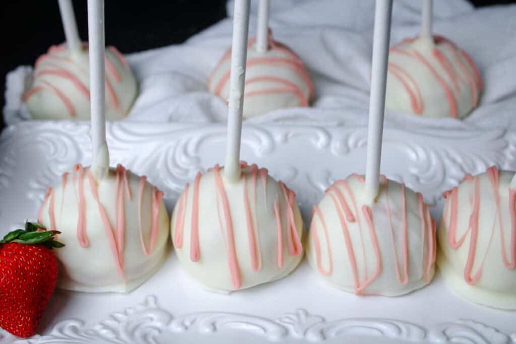 Strawberry cake pops coated with white chocolate and drizzled with pink candy coating .