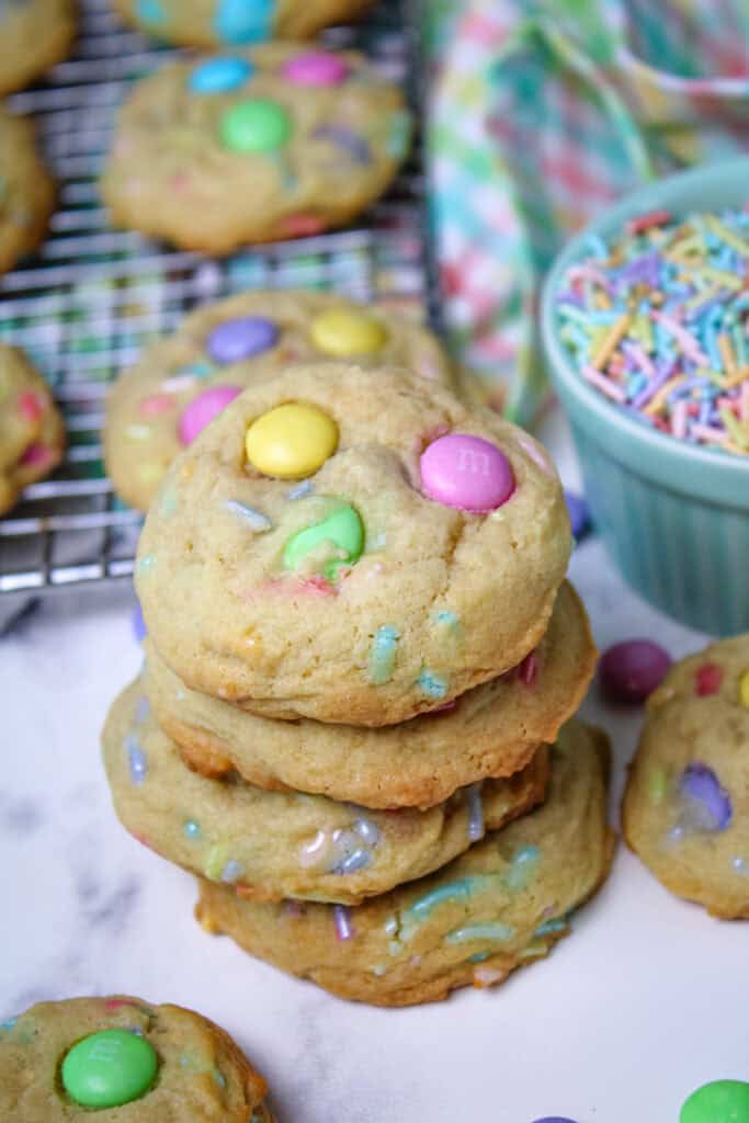 Funfetti Easter cookies in a stack next to a blue pastel bowl for a easter sprinkles surrounded by pastel M&Ms