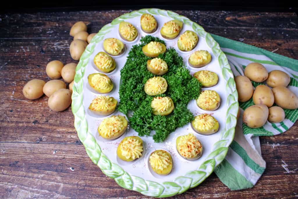 Deviled potatoes on a large egg platter with parsley in the middle . Surround by uncooked mini potatoes . 