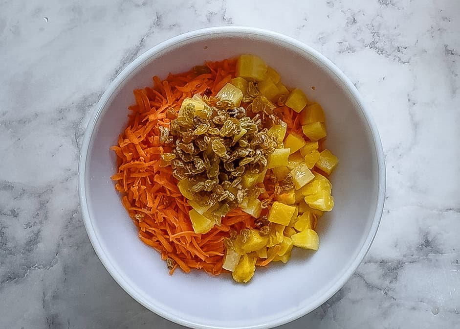 In a large mixing bowl shredded carrots , pineapple and raisins 