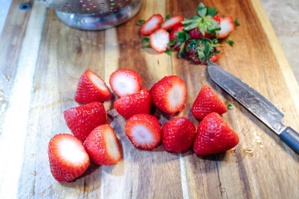 Strawberries on a cutting board with the tops sliced off 