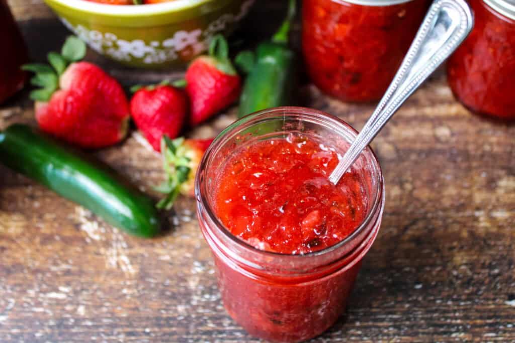 An open jar of strawberry jalapeno jam with a knife in it 