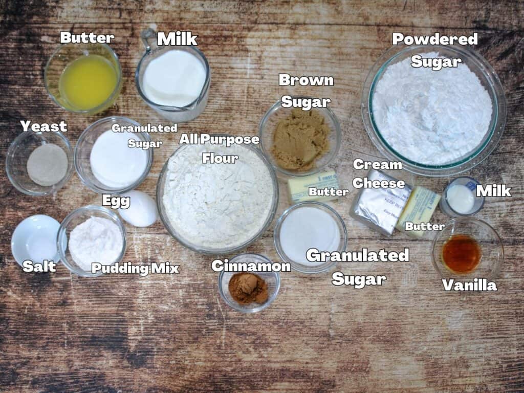 All of the ingredients for bread machine cinnamon rolls with them labeled . -Milk , butter , yeast , salt egg , pudding mix , flour , brown sugar , sugar , cinnamon , vanilla , cream cheese and powdered sugar .