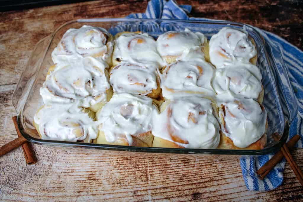 Bread machine cinnamon rolls in a baking dish with cream cheese frosting spread on top .