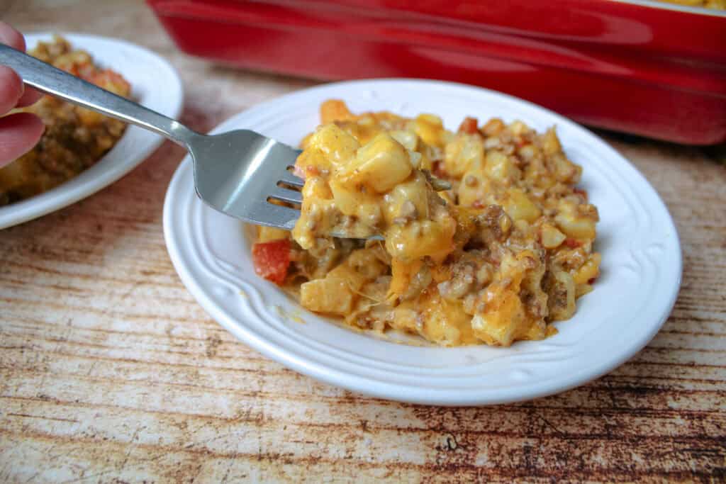 Close-up of a forkful of cheesy Taco Potato Casserole over a plate, showing the creamy texture with potatoes, ground beef, and melted cheese.