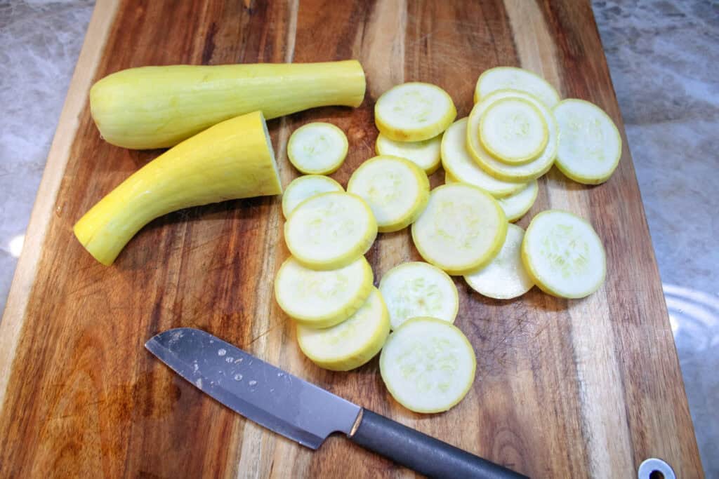 Fresh yellow summer squash sliced into rounds on a wooden cutting board with a knife.