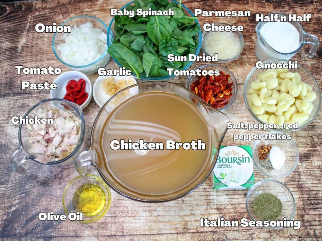 Overhead view of labeled ingredients for Marry Me Chicken Soup, including chicken broth, gnocchi, baby spinach, sun dried tomatoes, cooked chicken, onion, garlic, tomato paste, Boursin cheese, parmesan, olive oil, Italian seasoning, half and half, and spices on a rustic wood background.