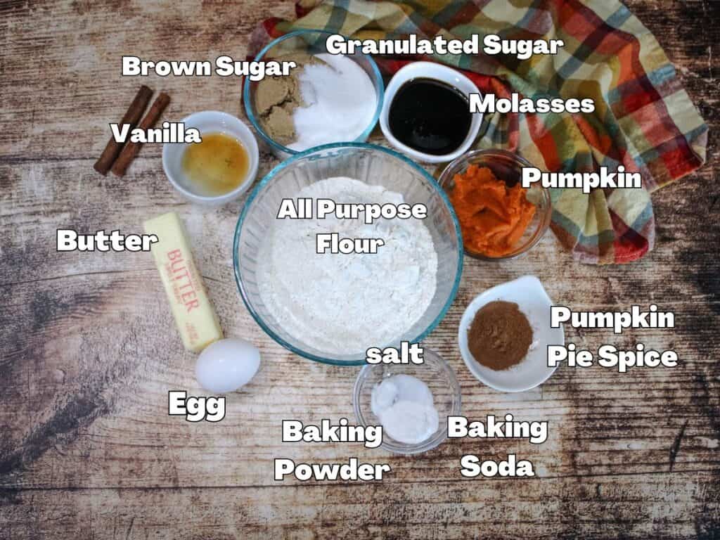 Pumpkin molasses cookie ingredients including butter, egg, flour, pumpkin puree, molasses, sugars, and pumpkin pie spice laid out on a rustic wooden table