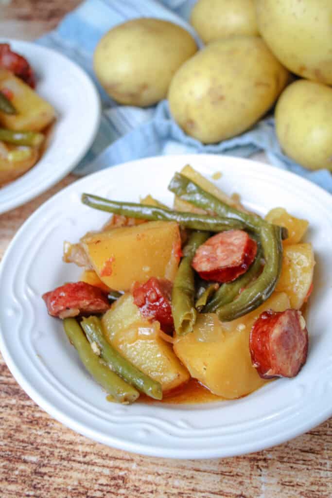 Close-up of a bowl of swamp potatoes with juicy smoked sausage, tender potatoes, and vibrant green beans in a savory sauce.


