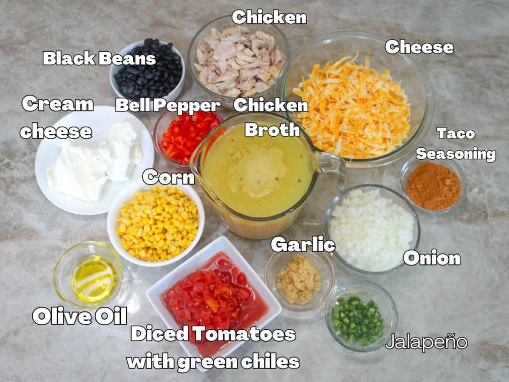 Overhead shot of chicken taco soup ingredients including shredded chicken, Colby Jack cheese, black beans, corn, cream cheese, onion, garlic, diced tomatoes with green chilies, jalapeño, taco seasoning, and chicken broth.