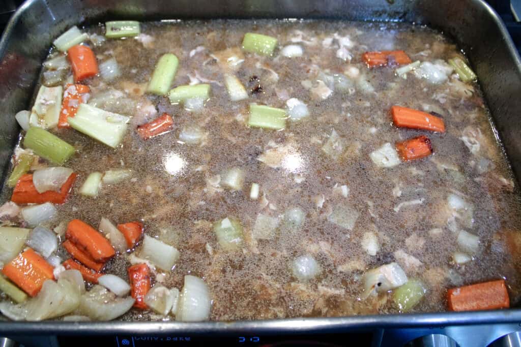 Turkey dripping in a roasting pan with carrots , celery and onions