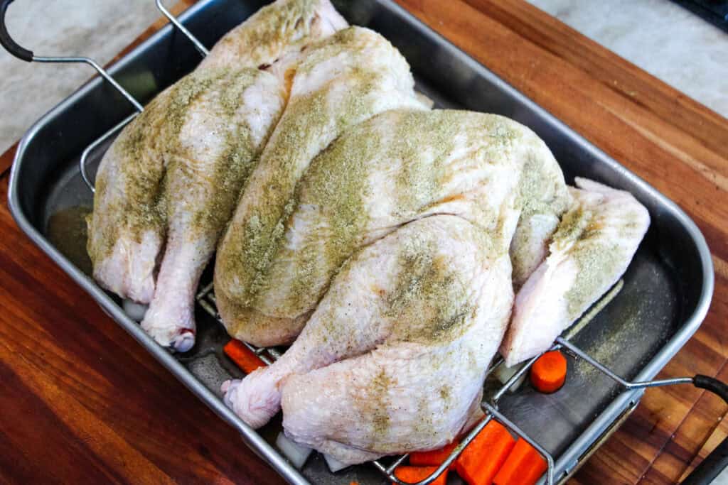 Seasoned raw spatchcock turkey resting on a roasting rack over carrots and onions, ready to go into the oven